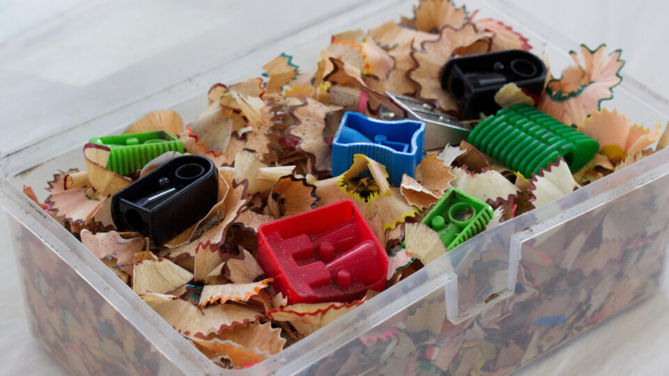 A box full of pencil shavings and six plastic pencil sharpeners in different colours and sizes.