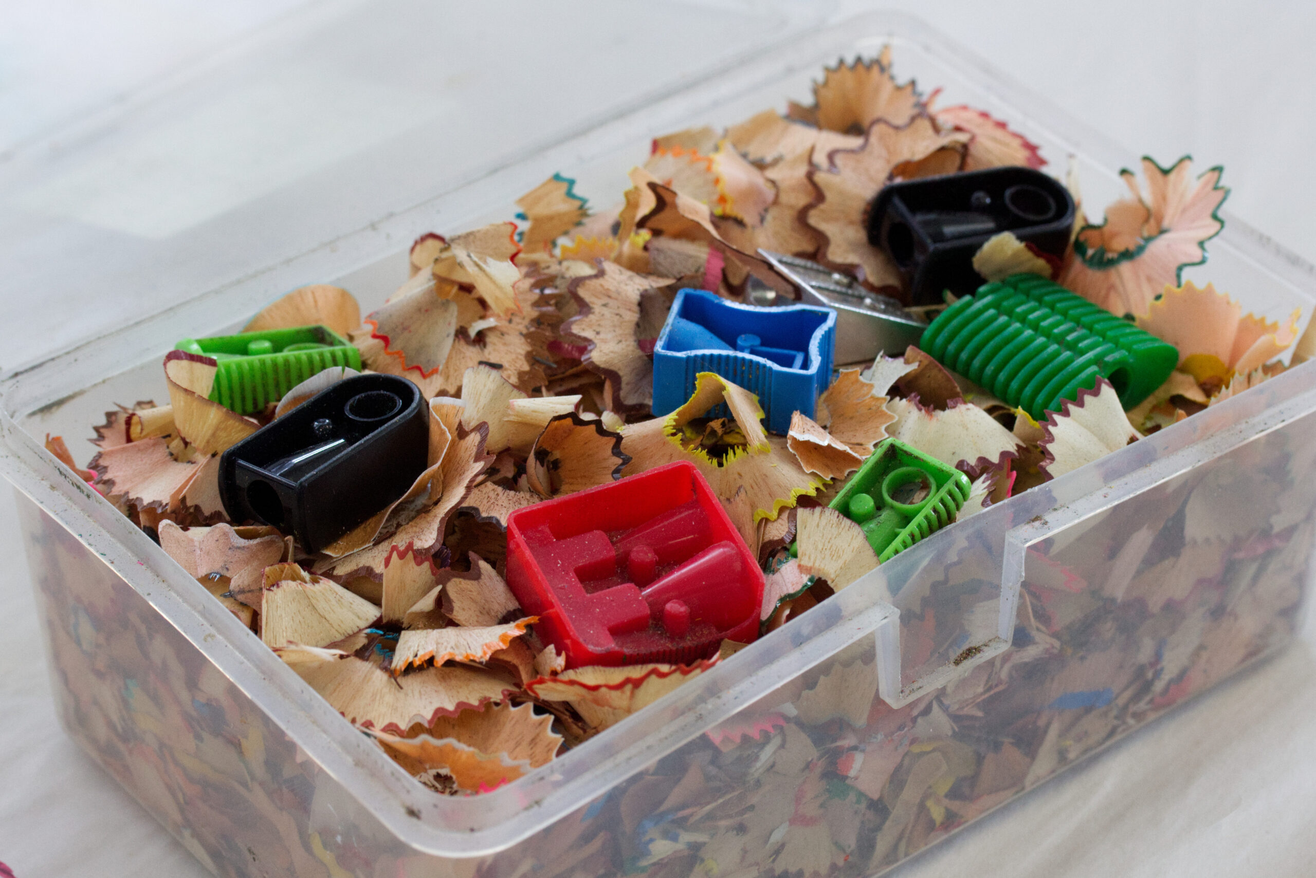 A box full of pencil shavings and six plastic pencil sharpeners in different colours and sizes.